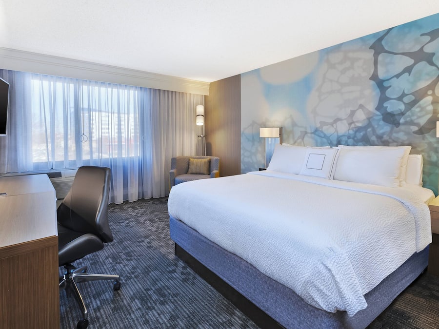 Een hotelkamer met een groot bed, een bureau, een stoel, een televisie en een raam met gordijnen.