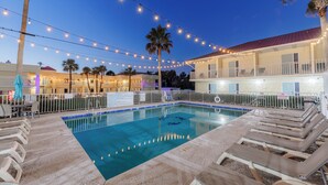 A swimming pool with lounge chairs, string lights, and a building with balconies. - Dunes Inn & Suites (Tybee Island)