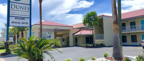 Un Dunes Inn & Suites con cielo despejado, palmeras y un estacionamiento.