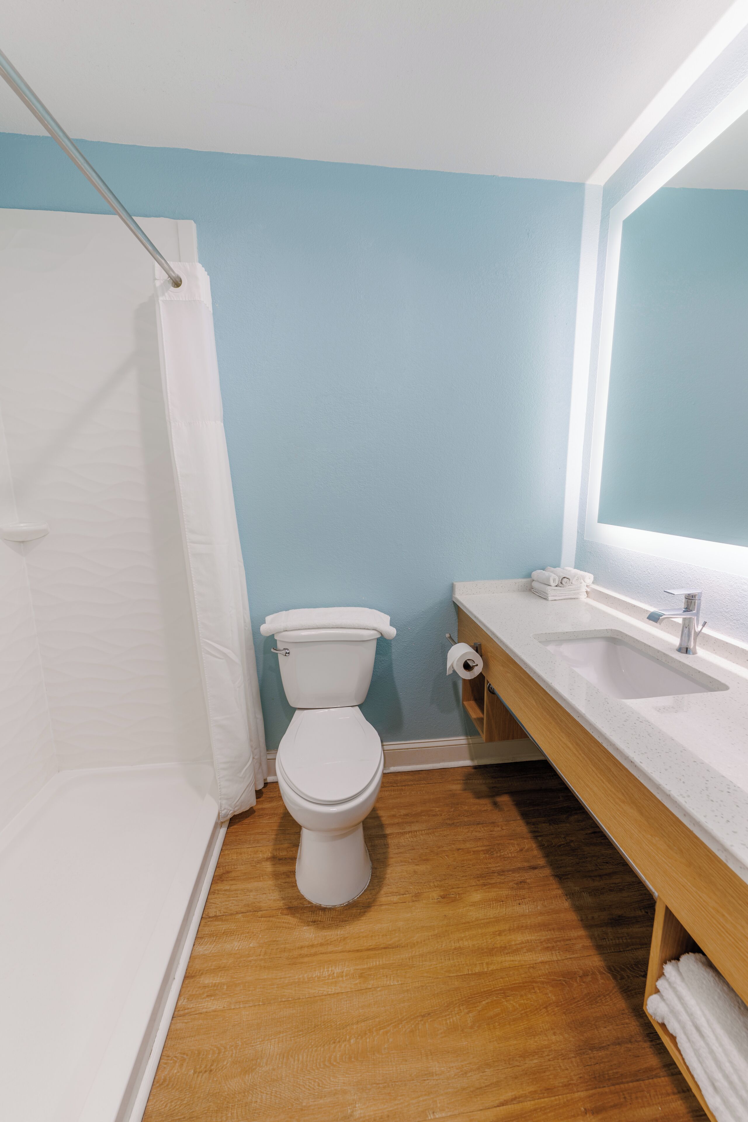 Une salle de bain avec des toilettes blanches, un meuble-lavabo en bois et un rideau de douche.