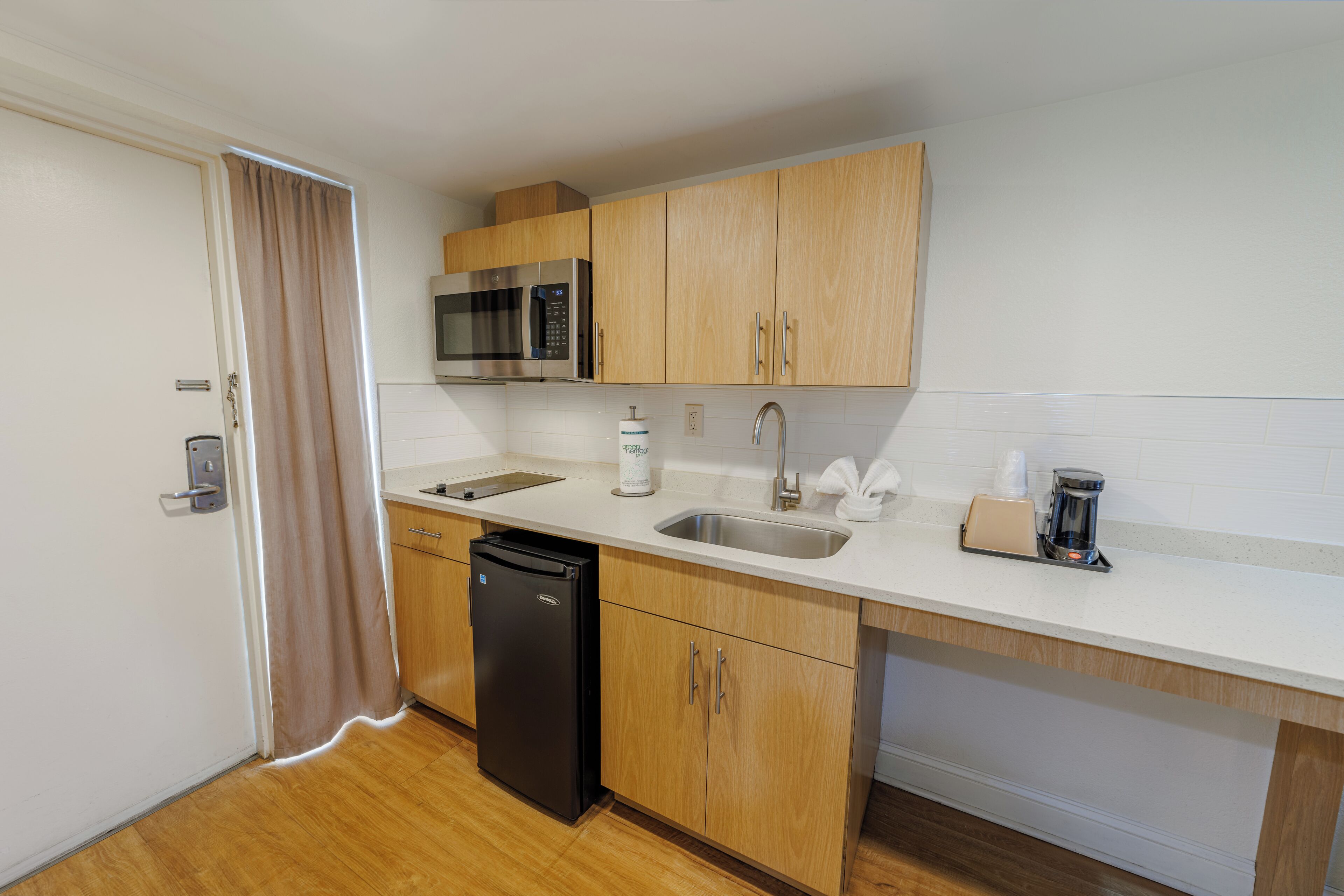 A compact kitchen with wooden cabinets, a stainless steel microwave, a sink, and a coffee maker.