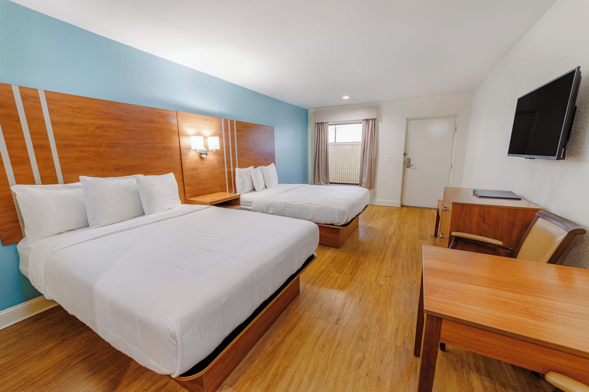 A hotel room with two beds, a desk, a chair, a TV, and a window with curtains.