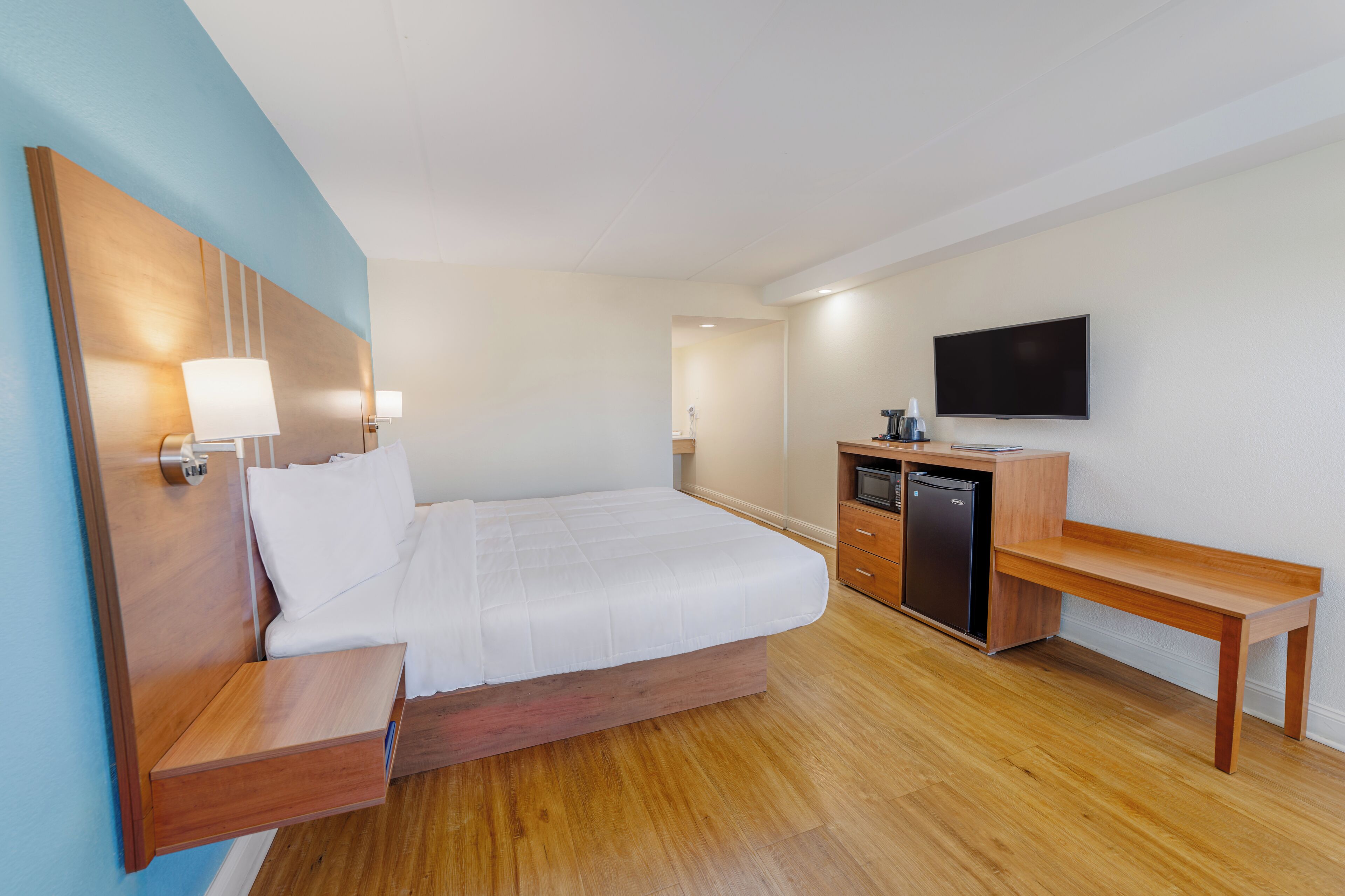 A hotel room with a bed, wooden desk, television, and a small kitchenette.