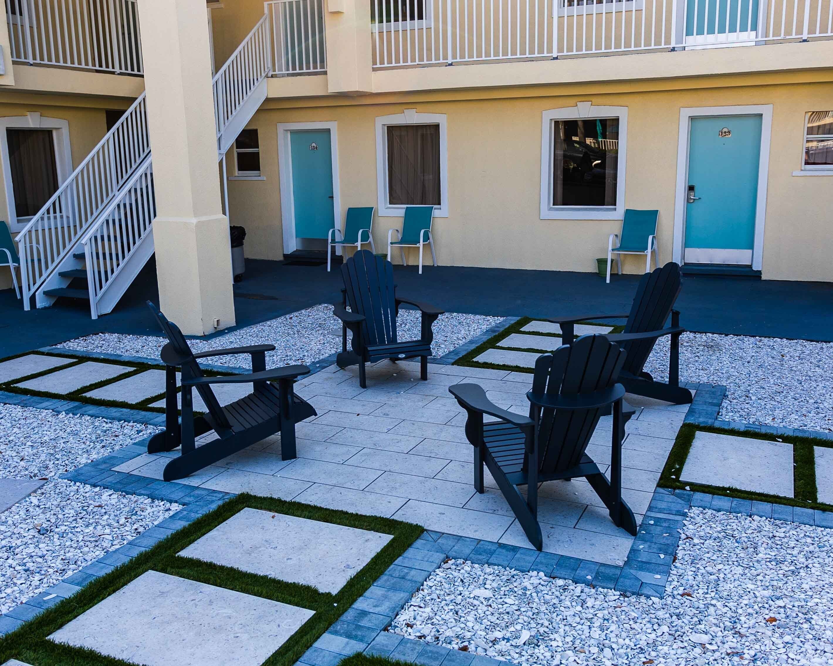An outdoor seating area with Adirondack chairs and a small table, surrounded by a patterned patio floor.