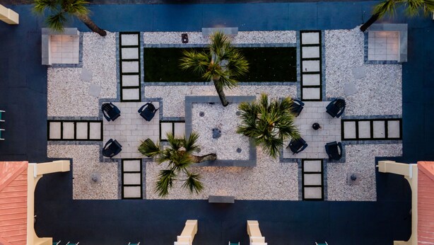 A rooftop terrace with a rectangular pool, surrounded by seating areas and palm trees. - Dunes Inn & Suites (Tybee Island)