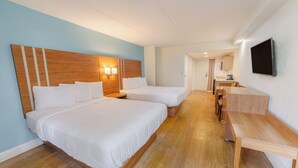A hotel room with two beds, a wooden headboard, a desk, and a TV mounted on the wall. - Dunes Inn & Suites (Tybee Island)