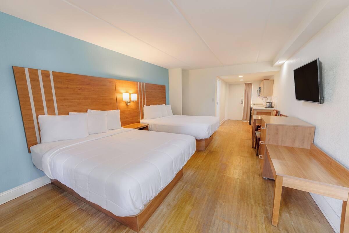 A hotel room with two beds, a wooden headboard, a desk, and a TV mounted on the wall.