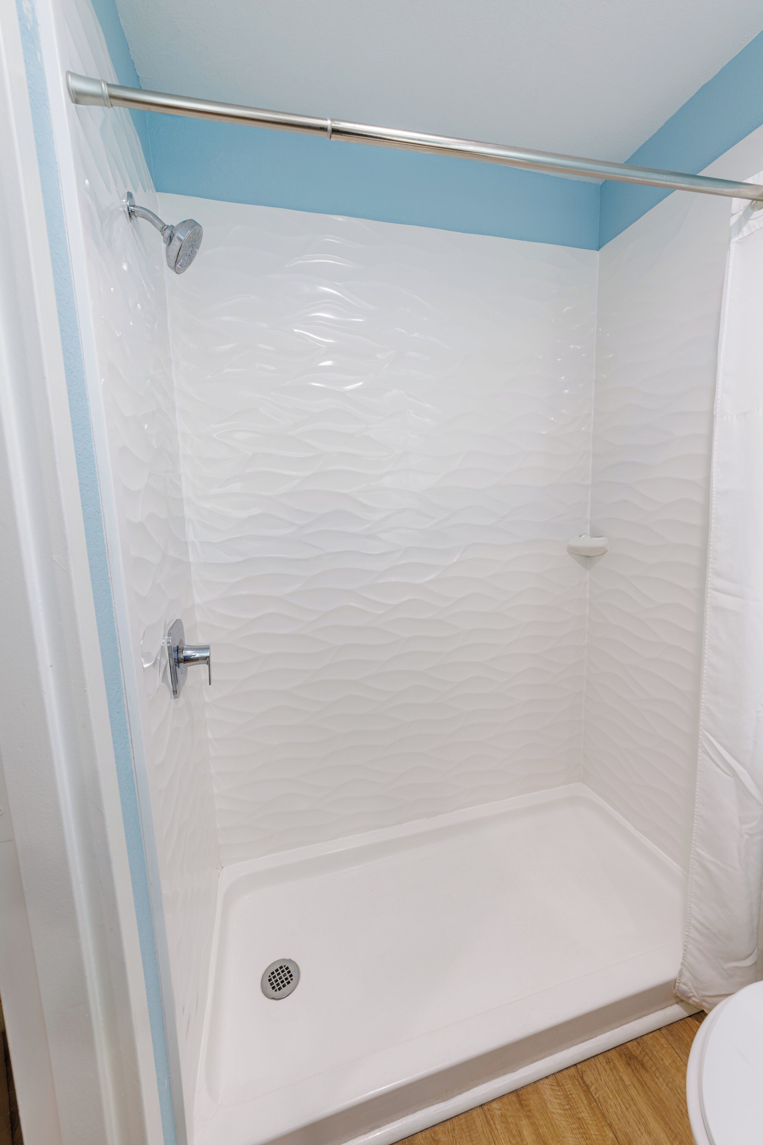 A shower with a white textured wall, a metal showerhead, and a shower curtain rod.
