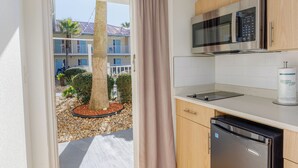 A compact kitchen with a microwave, dishwasher, and a view of a building with balconies and a palm tree outside. - Dunes Inn & Suites (Tybee Island)