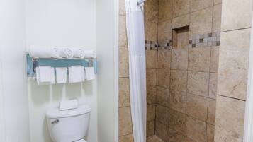 Casa de banho com sanita, chuveiro com parede revestida a azulejos e um porta-toalhas com toalhas.