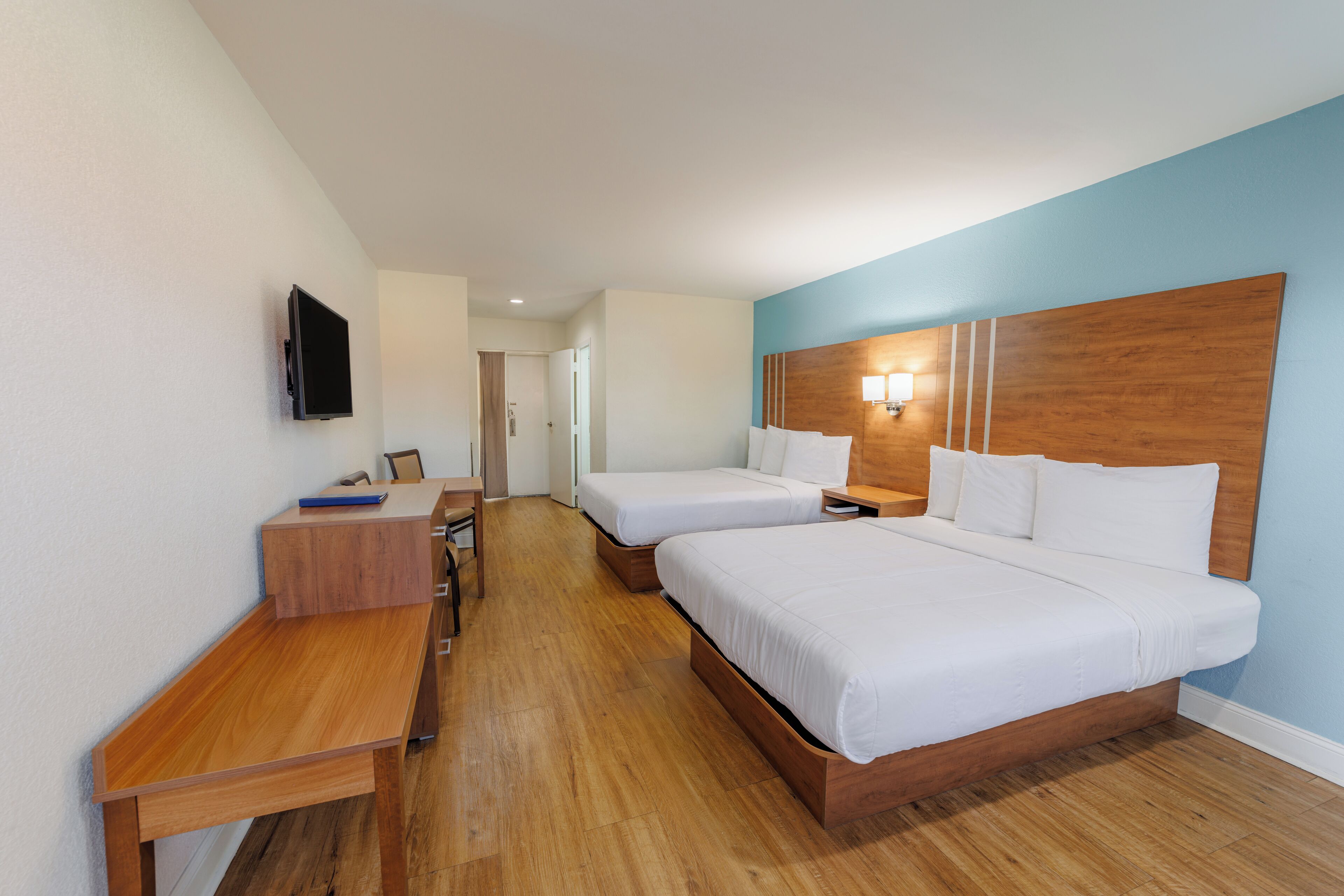 Een hotelkamer met twee enkele bedden, een houten bureau, een flatscreen televisie en een nachtkastje met een lamp.