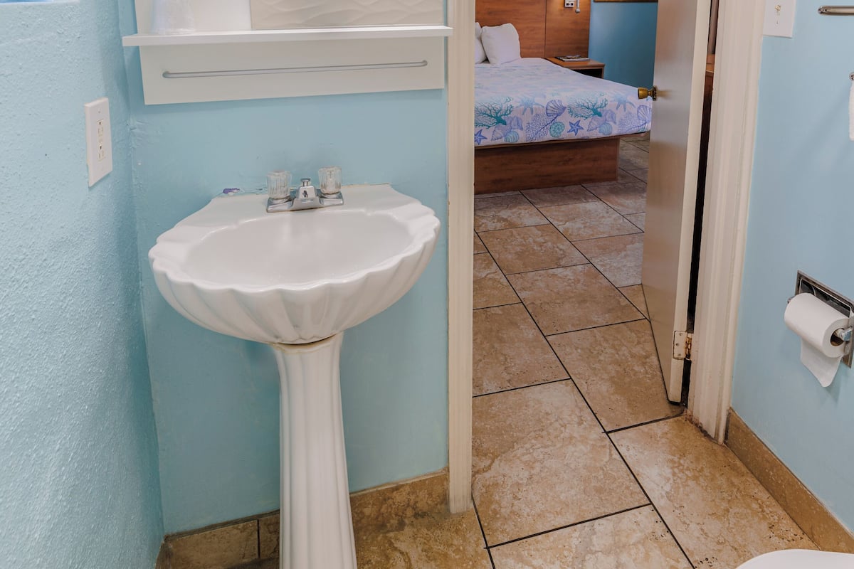 A bathroom with a pedestal sink, a mirror, and a shower area.