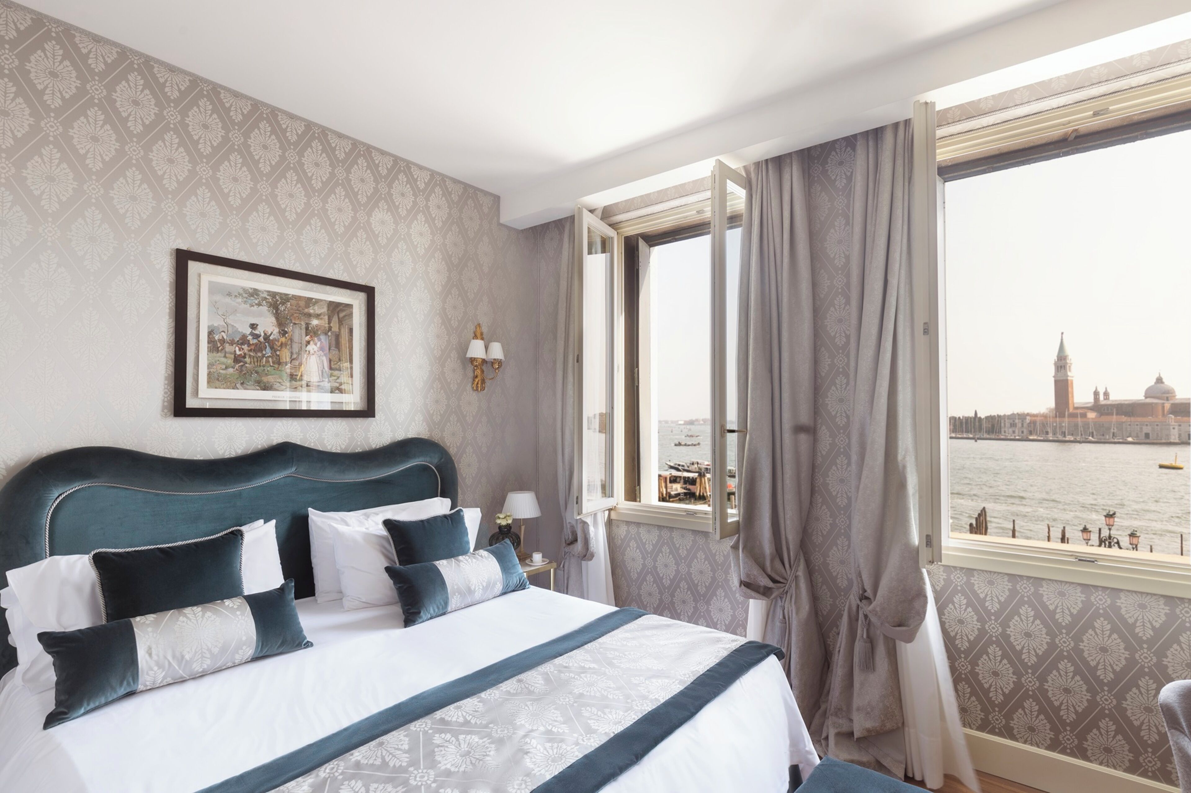 Ein Hotelzimmer mit einem großen Bett, Blick auf ein historisches Gebäude und einem mit Vorhängen versehenen Fenster.