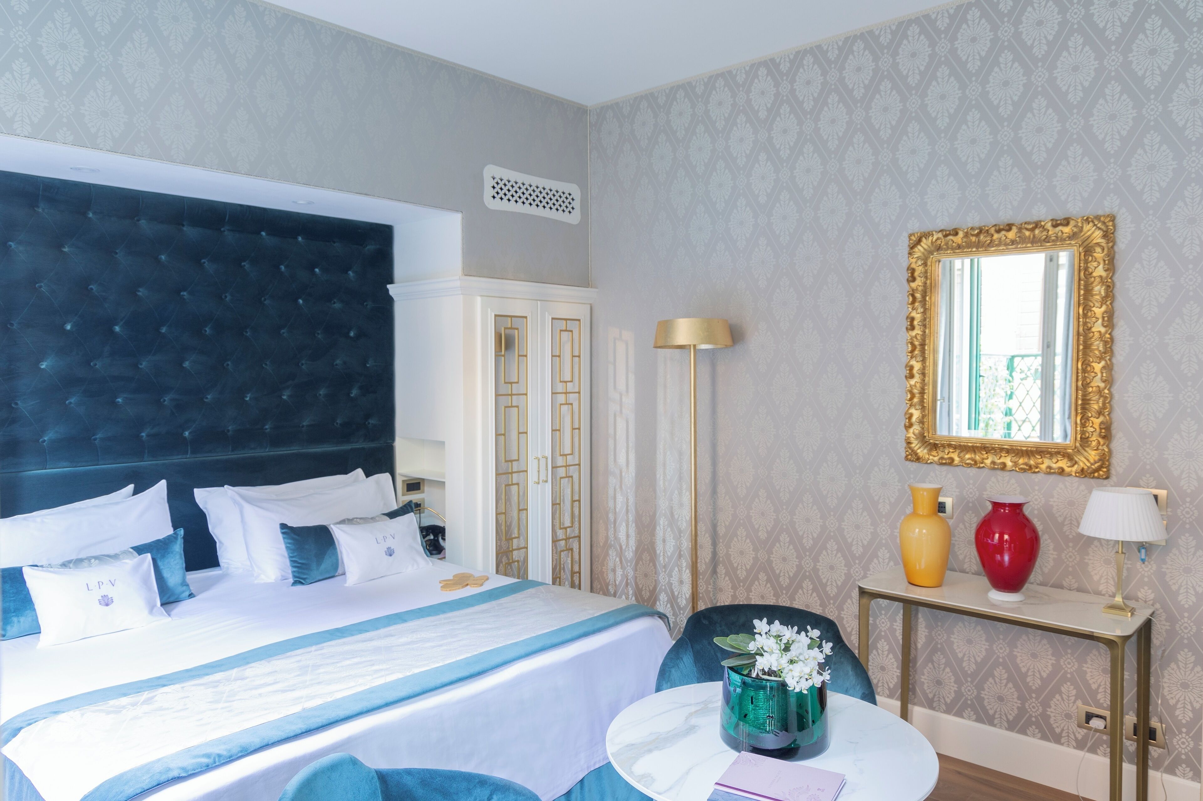 Une chambre d’hôtel avec un grand lit, une table de chevet avec une lampe, un miroir et des vases décoratifs.