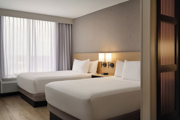 A hotel room with two beds, a large window with curtains, a wall-mounted light fixture, and a door with vertical blinds. - Hyatt Place Tampa Airport/Westshore (Tampa)