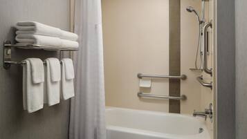 Un baño con bañera, un perchero con toallas dobladas, ducha con cabezal de ducha manual y barra de apoyo.