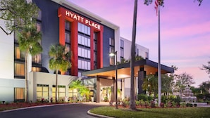 Un hotel moderno con un llamativo letrero de 'Hyatt Place', un acceso cubierto y un jardín ajardinado con una fuente.