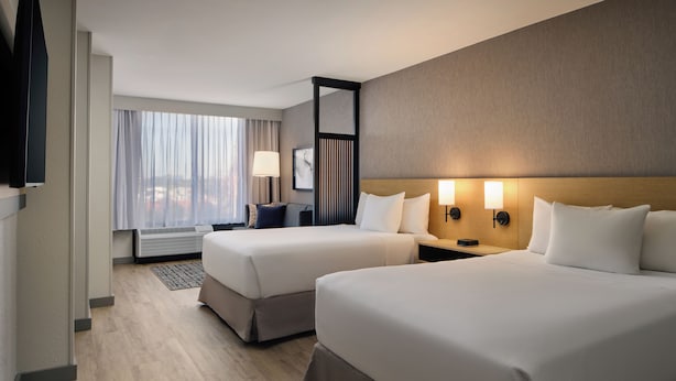 Habitación de hotel con dos camas, televisión, escritorio y vista a la ciudad.