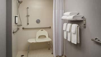 A bathroom with a shower, grab bars, a wheelchair-accessible bench, and a towel rack.