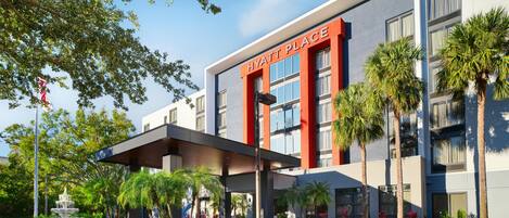 A modern hotel with a prominent 'Hyatt Place' sign, a covered entrance, and a landscaped garden with a fountain.
