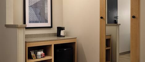 A small kitchenette with a coffee maker, a framed picture, and a mirror.