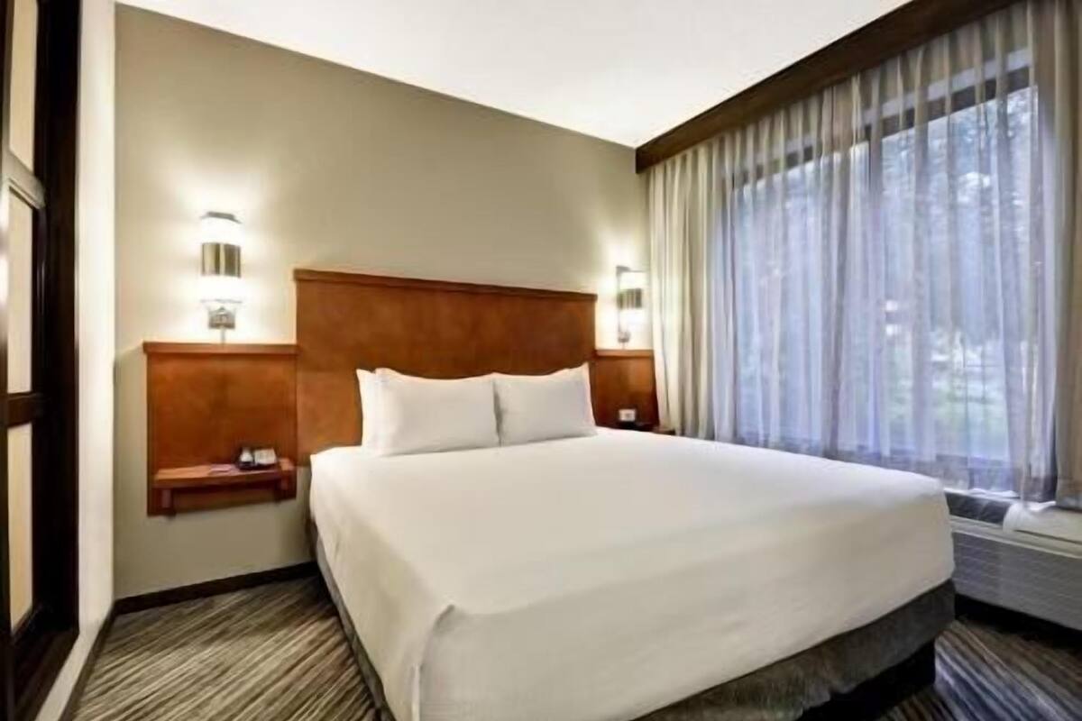 A hotel room with a large bed, two bedside tables, a headboard, and a window with curtains.