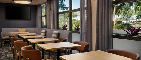 A hotel room with a large window, a flat-screen TV, a sofa, and multiple tables and chairs.