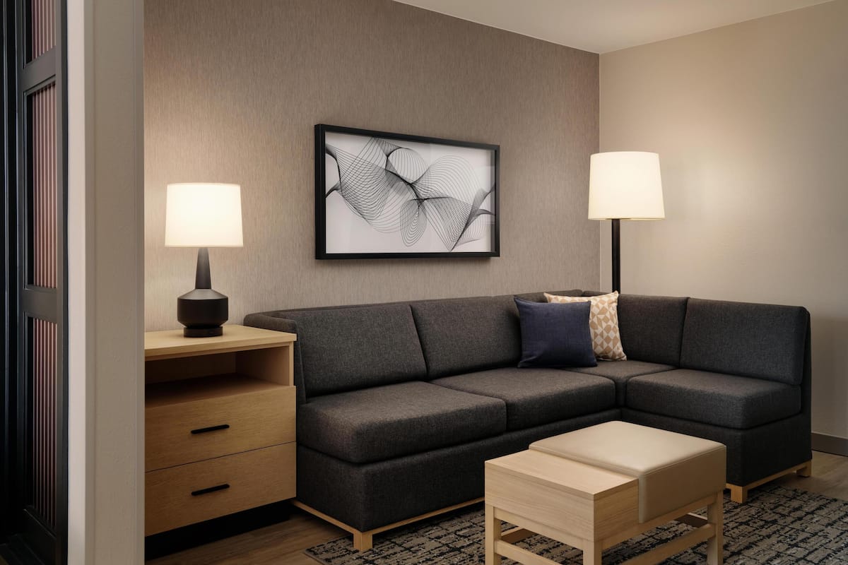A modern living room with a sectional sofa, a side table, a lamp, and a framed abstract artwork on the wall.