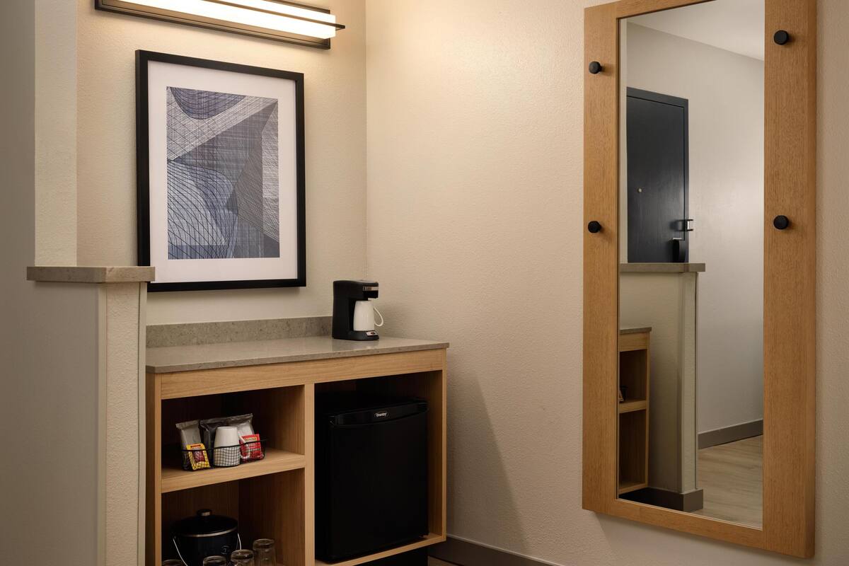 A kitchenette with a coffee maker, a framed picture, and a mirror.