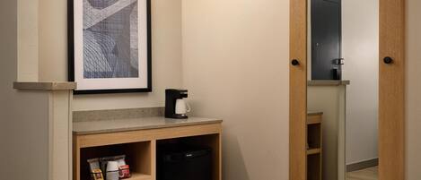 A kitchenette with a coffee maker, a framed picture, and a mirror.
