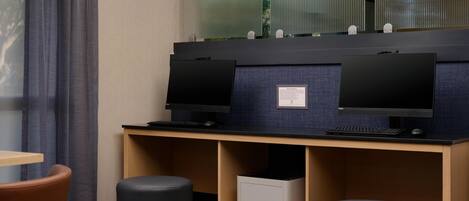 Una habitación de hotel con un escritorio, dos monitores, una impresora y una silla.