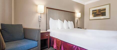 A hotel room with a bed, a chair, a nightstand, and a wall-mounted lamp.