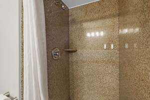 Ducha con pared de granito, cortina blanca y cabezal de ducha cromado.