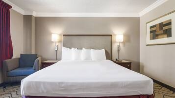 Una habitación de hotel con una cama grande, dos mesitas de noche, una silla y dos lámparas de pared.