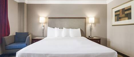 Une chambre d’hôtel avec un grand lit, deux tables de chevet, une chaise et deux lampes fixées au mur.
