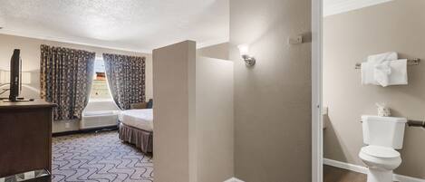 Habitación de hotel con cama, escritorio, silla, ventana con cortinas, baño con inodoro y zona de ducha.