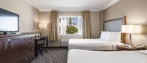 Quarto de hotel com duas camas, uma mesa de trabalho com televisão, uma luminária e uma janela com cortinas.