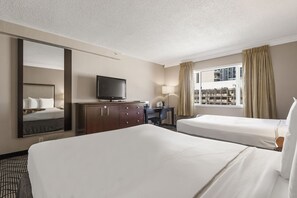 A hotel room with two beds, a TV, a desk with a chair, and a large mirror.