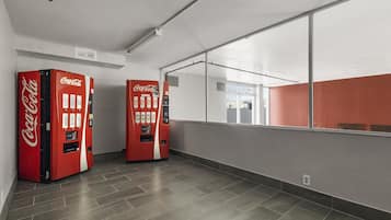 Un intérieur moderne avec deux distributeurs automatiques de Coca-Cola rouges, un sol carrelé gris et un grand miroir qui reflète un mur rouge et une fenêtre.