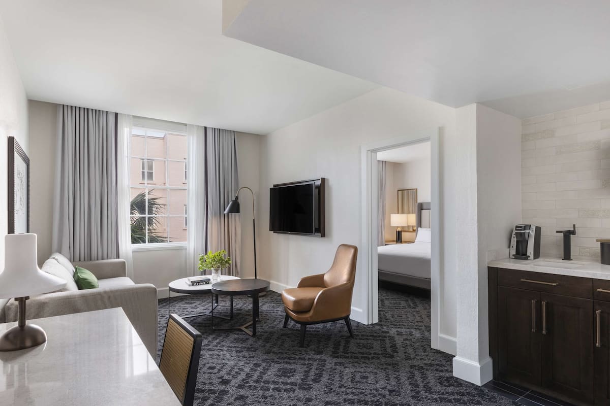 A modern hotel room with a sofa, armchair, dining table, and a TV.