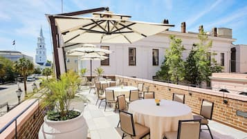 An outdoor patio with round tables and chairs, a brick wall, and a view of a white building with a clock tower.