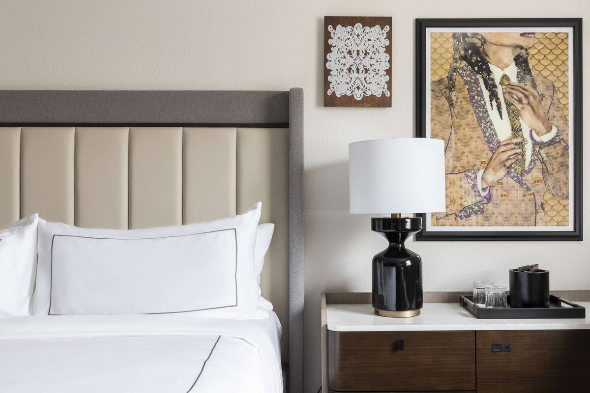 A hotel room with a bed, a nightstand, a lamp, and two framed artworks on the wall.