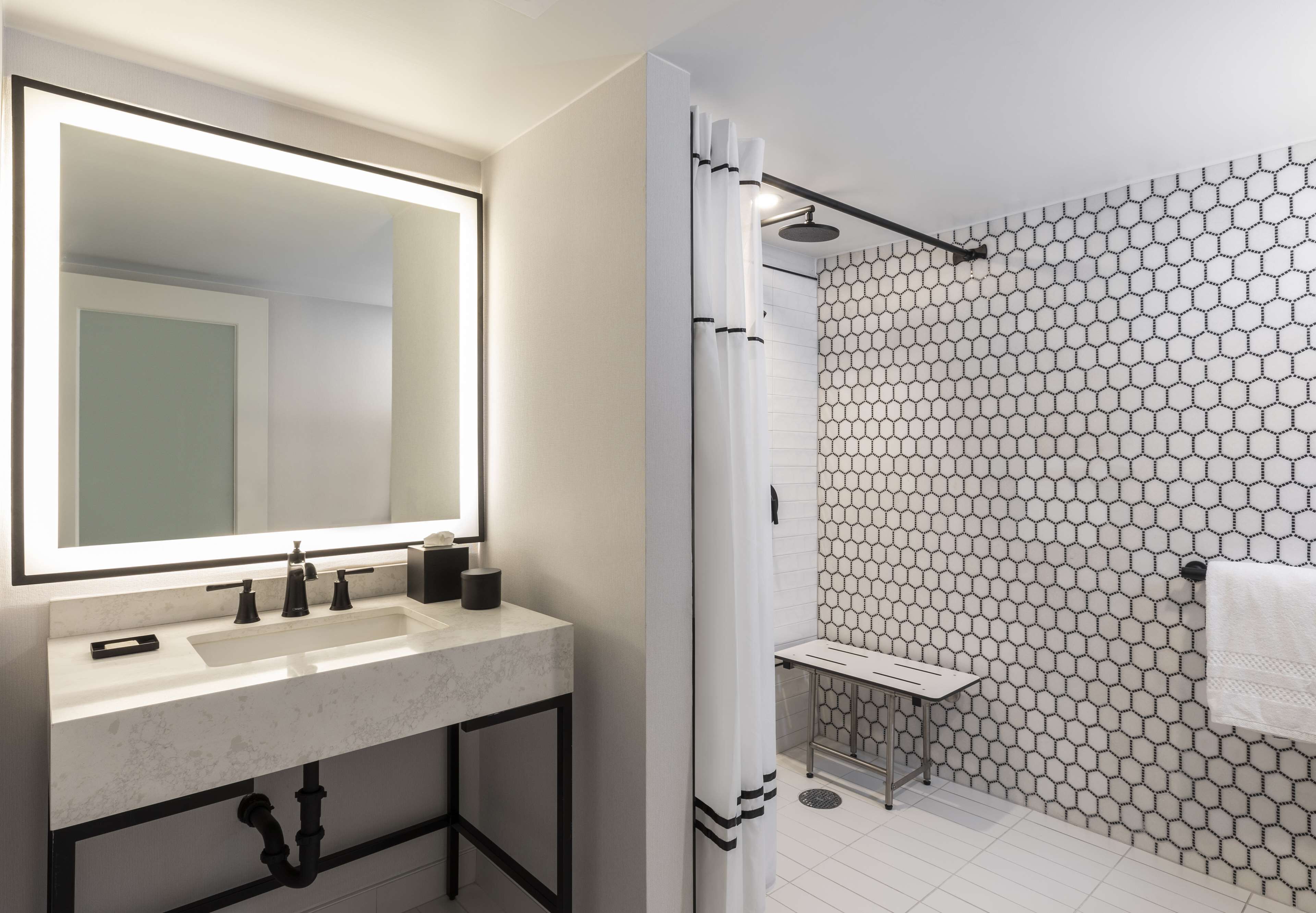 A modern bathroom with a large mirror, a sink, and a shower with a hexagonal tile pattern.