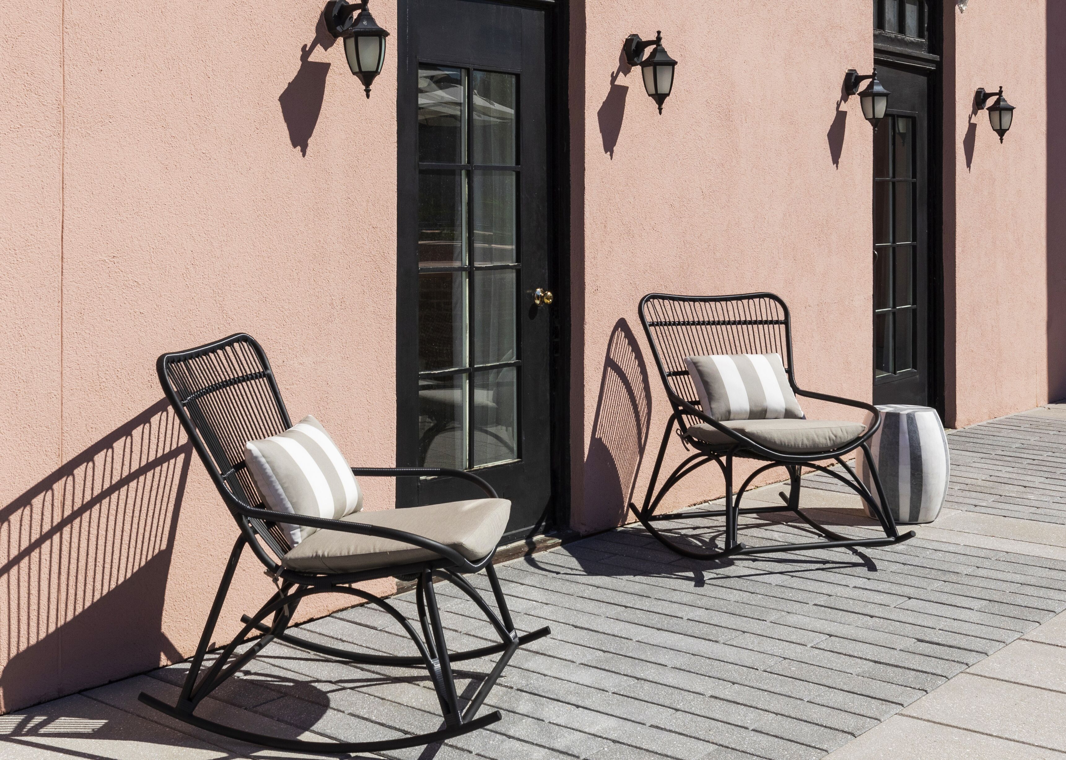 Two rocking chairs with cushions against a building facade with a door and windows.