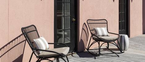 Two rocking chairs with cushions against a building facade with a door and windows.