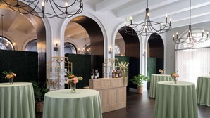 A room with multiple round tables covered with green tablecloths, a bar area with a green backdrop, and arched ceiling with chandeliers. - Mills House Charleston, Curio Collection by Hilton (Charleston)
