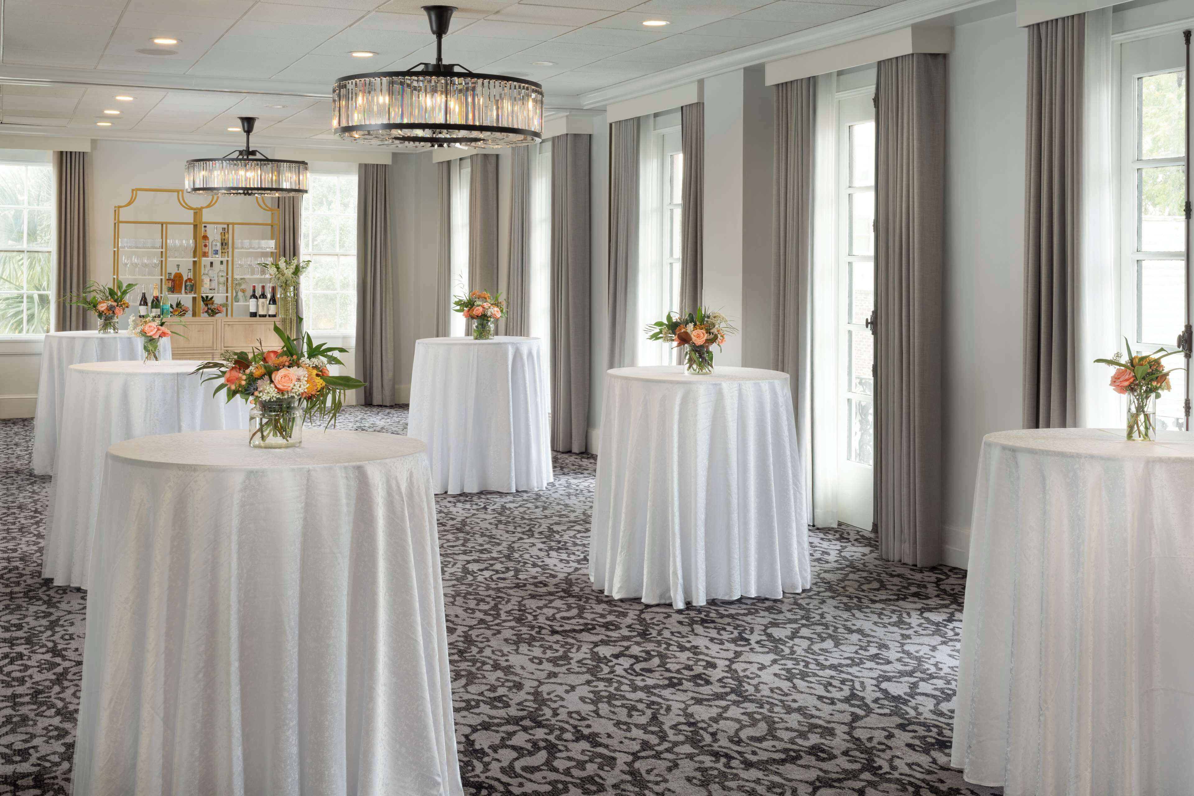 A hotel room with round tables covered in white tablecloths, each with a floral centerpiece.