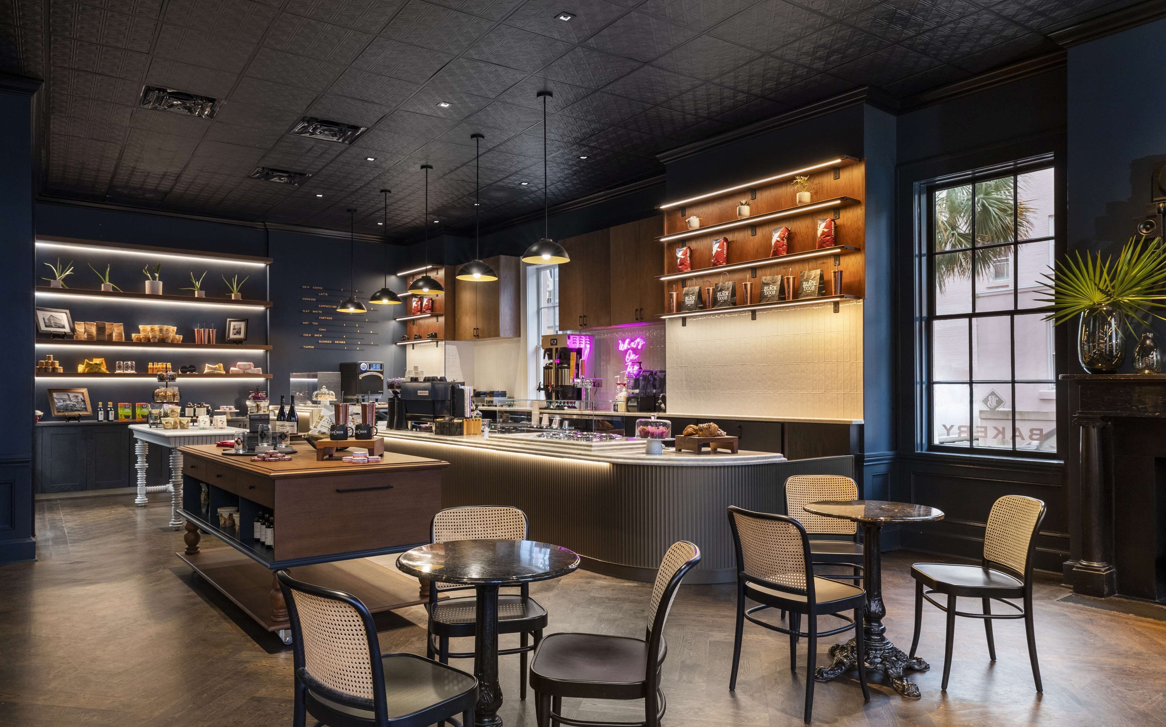 A modern cafe interior with a central bar, seating area, and shelves displaying coffee and tea.