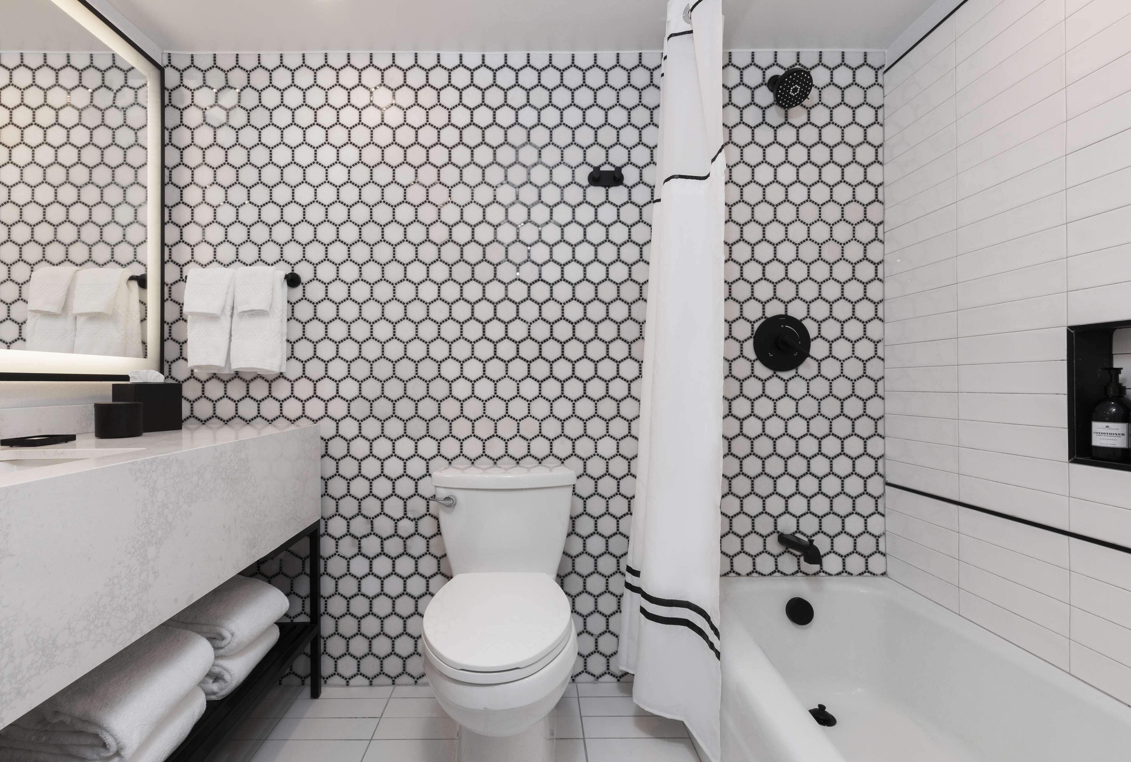 Ein Badezimmer mit sechseckischem Fliesenmuster, einer Toilette, einem Waschbecken mit Spiegel und einer Badewanne.