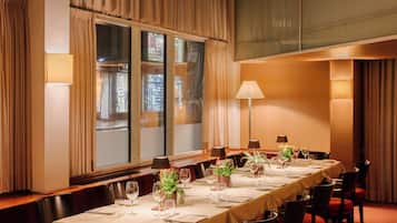 A conference room with a long table set for a meeting, large windows with curtains, and a carpeted floor.